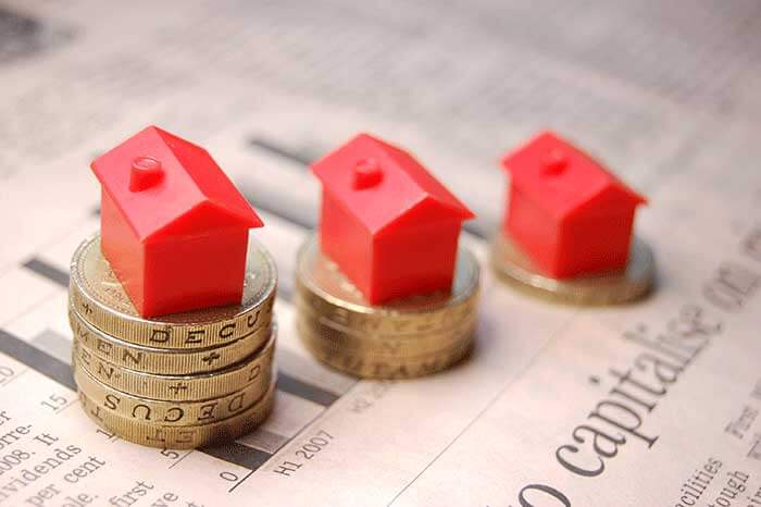 Three red toy houses stood on stacks of pound coins