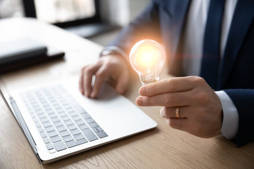 Close up of a business person sitting on a desk holding a light bulb