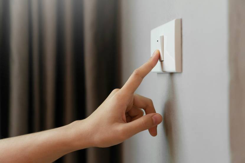 A hand flicking off a light switch with a dark curtain in the background