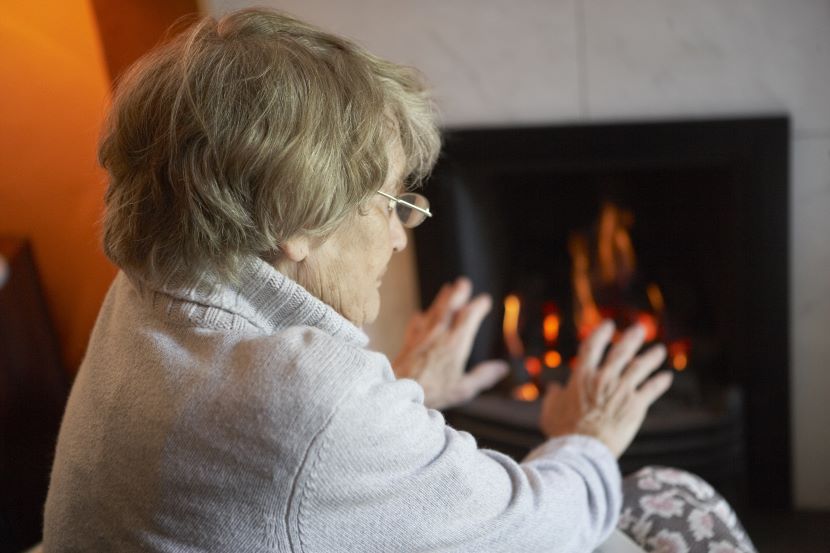 Older woman warming her hands by a fire 