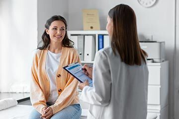 A woman sits in a chair while a doctor speaks to her, discussing her health in a comfortable setting.
