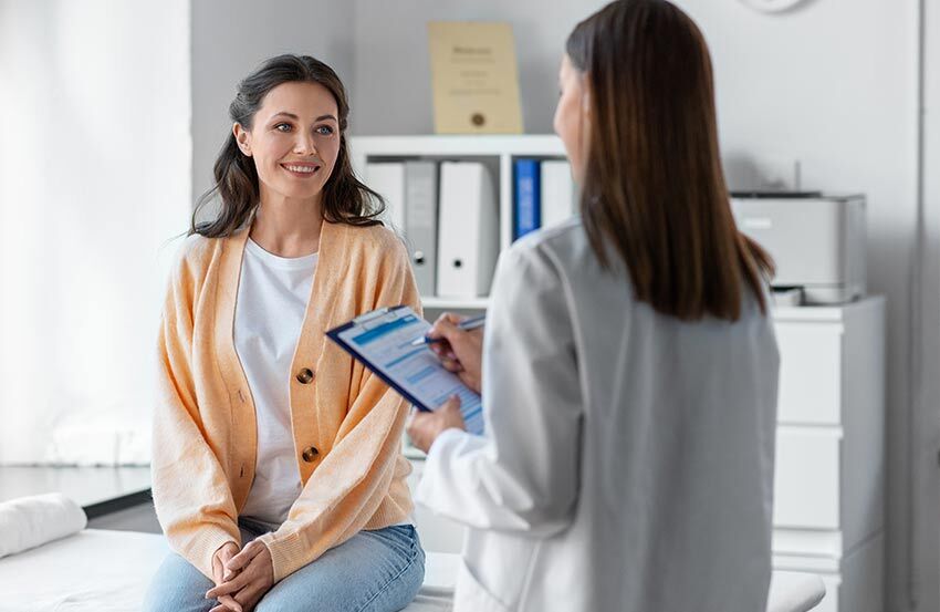 A woman sits in a chair while a doctor speaks to her, discussing her health in a comfortable setting.