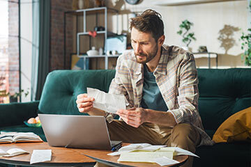 Man sitting at home with a laptop, dealing with financial issues following a death in the family
