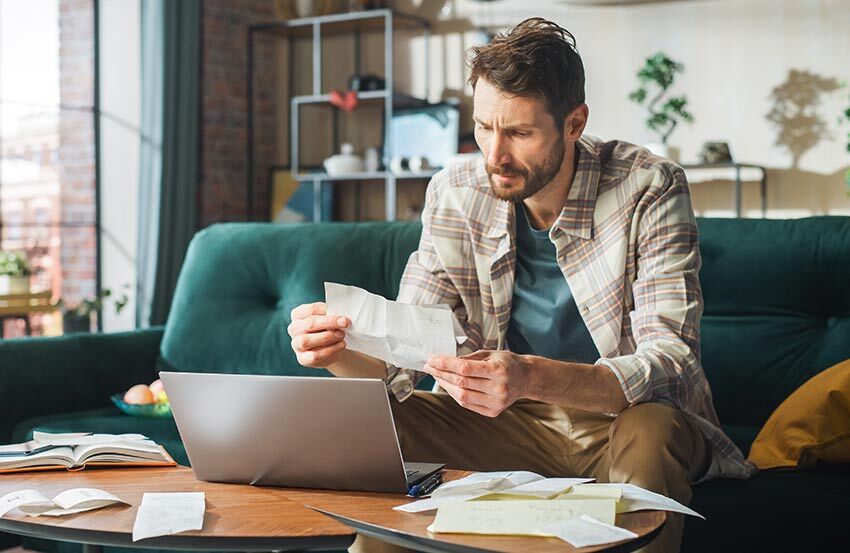 Man sitting at home with a laptop, dealing with financial issues following a death in the family.
