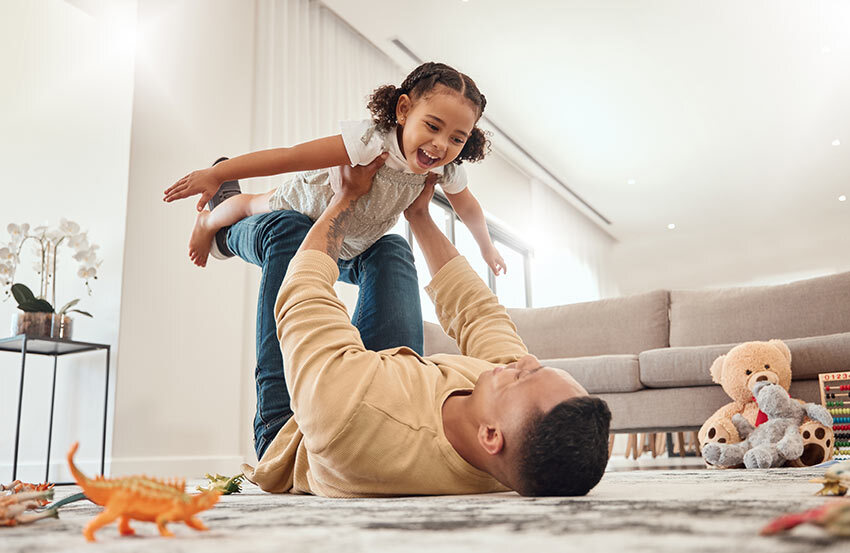 A man and a child happily playing together on the floor in a cozy living room, enjoying quality family time