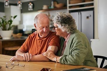 An older couple enjoying a meal together at a kitchen table, smiling and engaged in conversation.