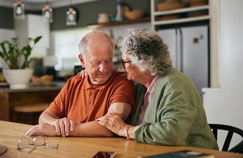 An older couple enjoying a meal together at a kitchen table, smiling and engaged in conversation.
