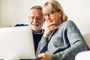 An older couple sitting on a couch, smiling as they look at a laptop, discussing inheritance tax matters together.