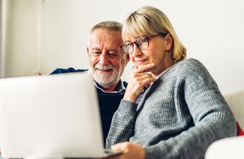 An older couple sitting on a couch, smiling as they look at a laptop, discussing inheritance tax matters together.