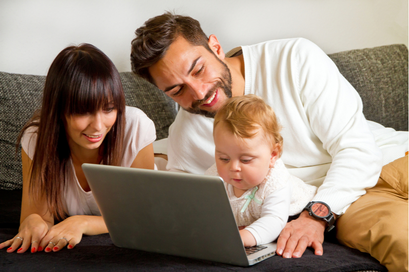 A couple and a baby huddle around a laptop on a sofa