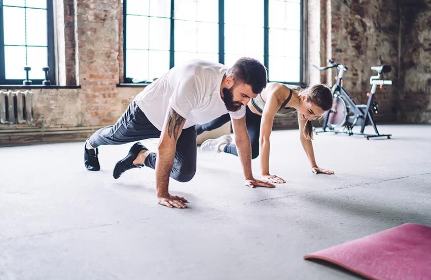 A man and woman performing push-ups side by side in a gym, focused on their workout routine.
