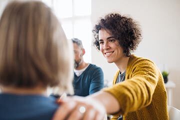 A woman shakes hands with another woman, both smiling and engaged in a friendly conversation.
