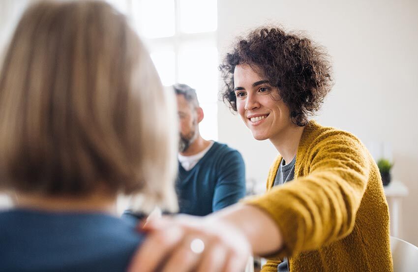 A woman shakes hands with another woman, both smiling and engaged in a friendly conversation.