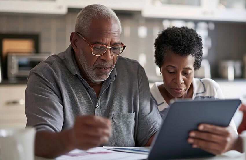 An older couple smiles while looking at a tablet together, sharing a moment of connection and discovery