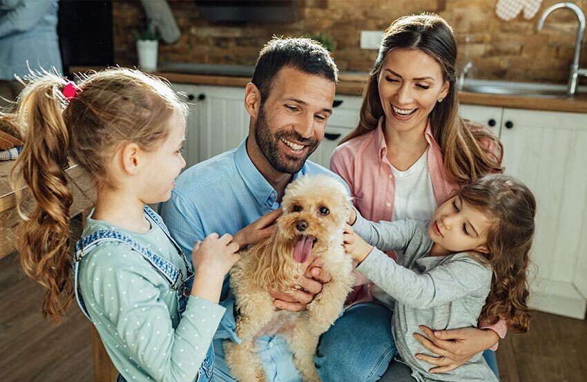 A happy family stands in their kitchen with a playful dog, enjoying a warm moment together.
