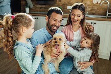 A happy family stands in their kitchen with a playful dog, enjoying a warm moment together.