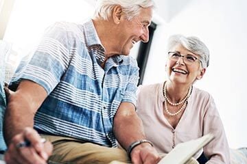 An older couple sits together on a couch, happily sharing a book and enjoying each other's company.