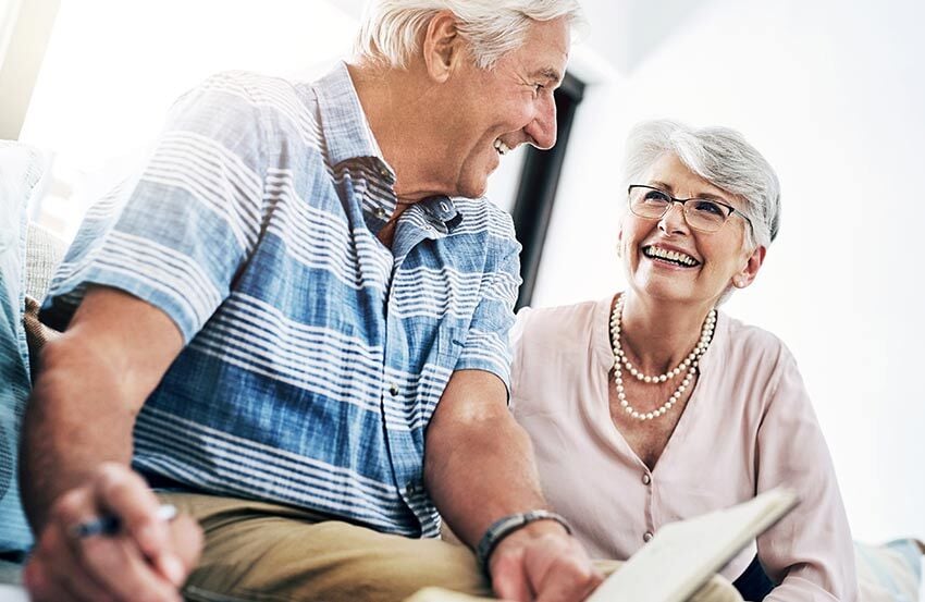 An older couple sits together on a couch, happily sharing a book and enjoying each other's company.