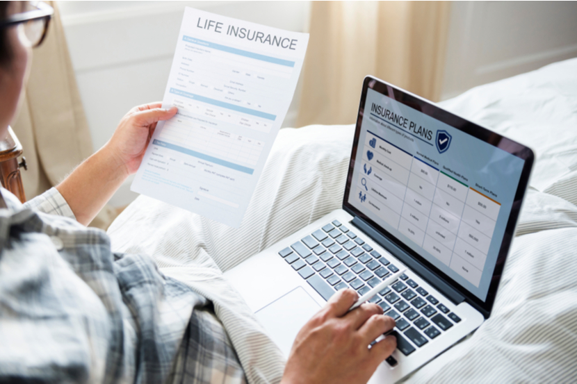 A person looking at life insurance plans on their laptop and holding a life insurance form