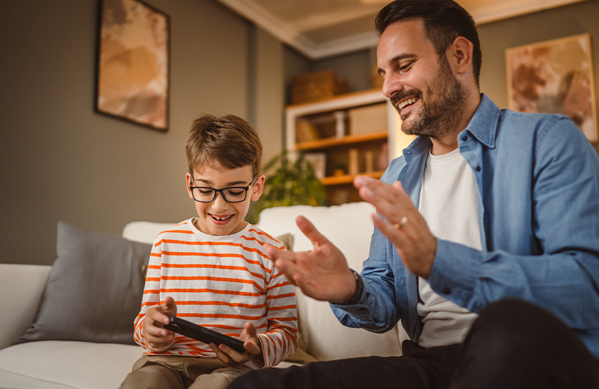 A father and son joyfully playing video games together, sharing smiles and excitement in their living room.