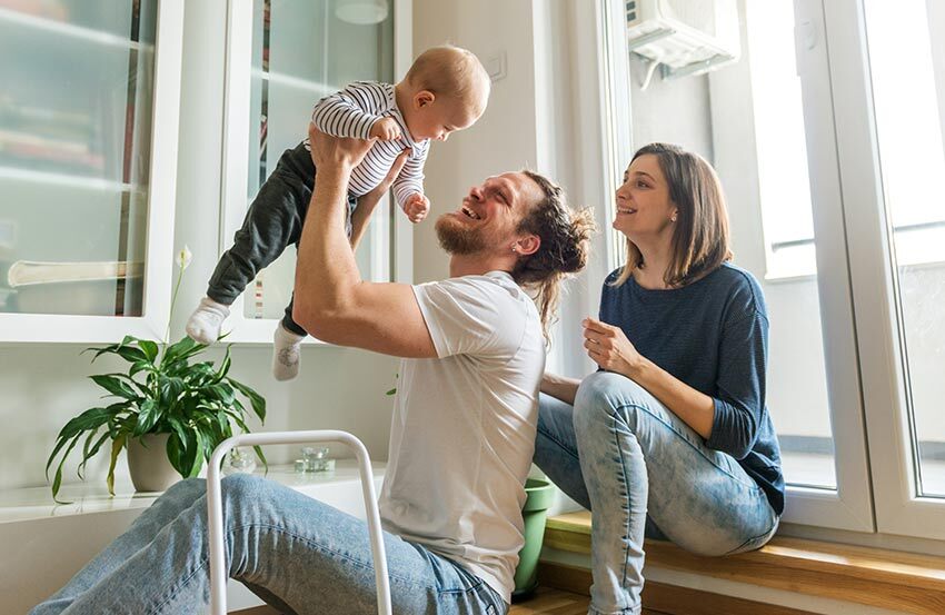 A man and woman sit on the floor, smiling at a baby between them, creating a warm and loving family moment.