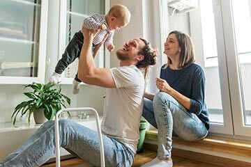 A man and woman sit on the floor, smiling at a baby between them, creating a warm and loving family moment.