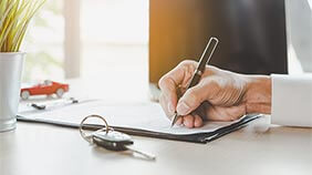 Person signing a logbook loan agreement with a car key in the foreground