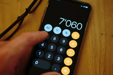 Close-up of a smartphone calculator app with hand on wooden desk.