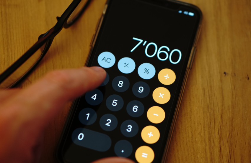 Close-up of a smartphone calculator app with hand on wooden desk