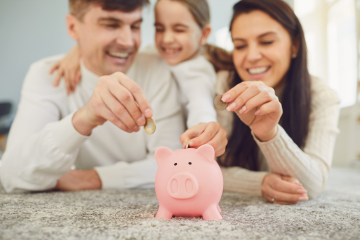 Dad, daughter and mum putting coins into a piggy bank