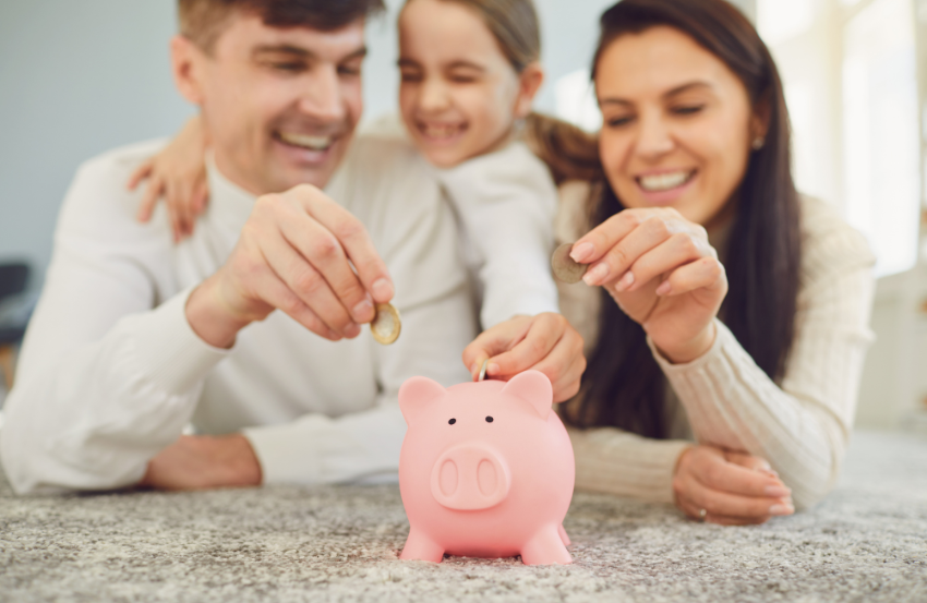 Dad, daughter and mum putting coins into a piggy bank