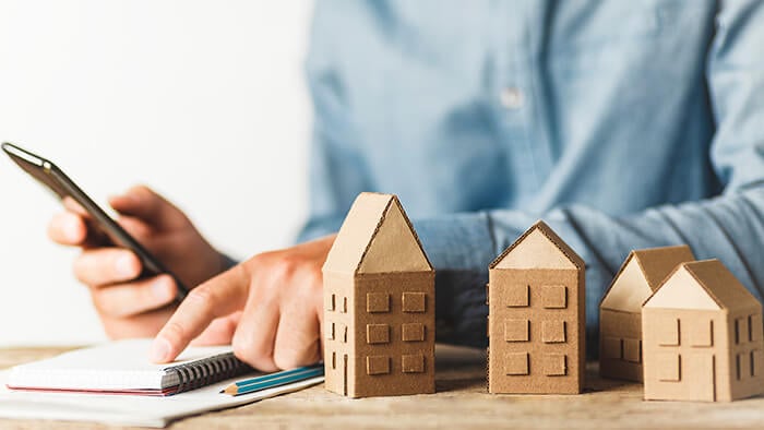 Person calculating their finances with wooden houses in the foreground