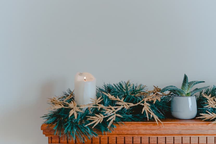 A candle on a mantle with a Christmas foliage decorating it