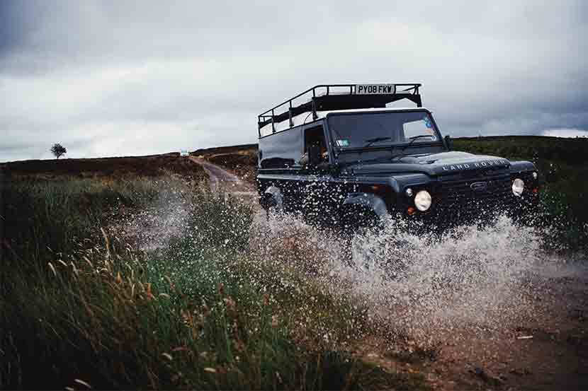 Land Rover Defender off-roading on green lane through a puddle