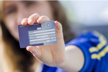 A woman holding up a blue EHIC card