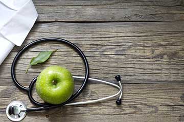 A green apple and a stethoscope on a wooden table