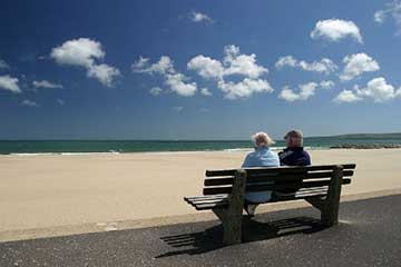 An elderly couple sat on a bench overlooking a beach