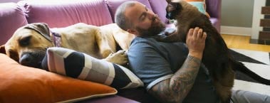 Man holding a cat with a dog lying next to him