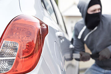 A person wearing a balaclava breaking into a car