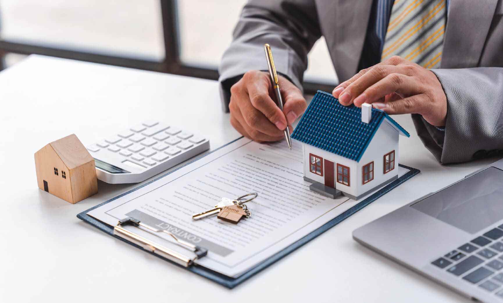 A person holding a small model house while writing on a form on a clipboard